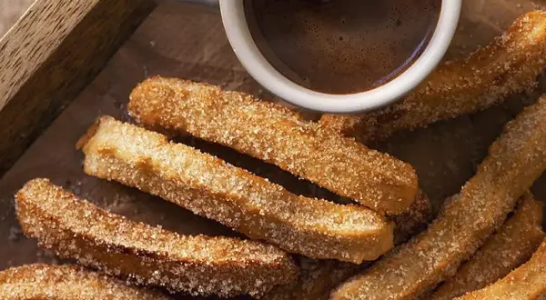 Churros caseros espolvoreados con azúcar junto a una taza de chocolate caliente.