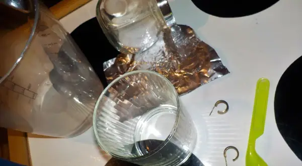Szklanka, folia aluminiowa, sól, łyżeczka i kolczyki na blacie.