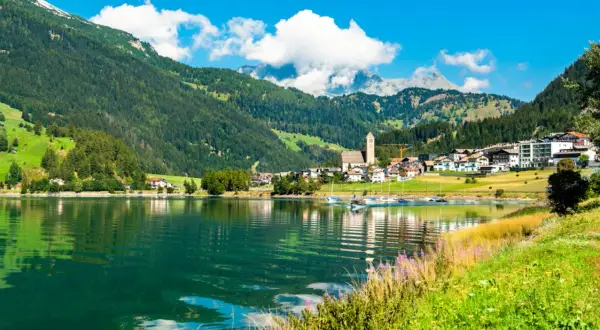 Incantevole lago alpino con barche a vela, circondato da verdi montagne e pittoreschi borghi Trentino Alto Adige.