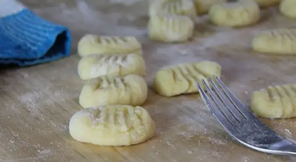 Frisch geformte Gnocchi liegen auf bemehltem Holz. Eine Gabel und ein blauer Lappen deuten darauf hin, dass das Gnocchi selber machen gerade erst begonnen hat.