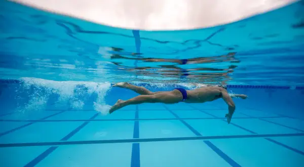 Underwater view of a swimmer performing flutter kicks, propelling through the blue pool water.
