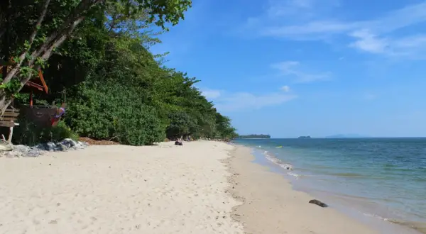 En avkopplande stranddag på Koh Jum. Lång, vit sandstrand kantad av frodig grönska och turkost hav.