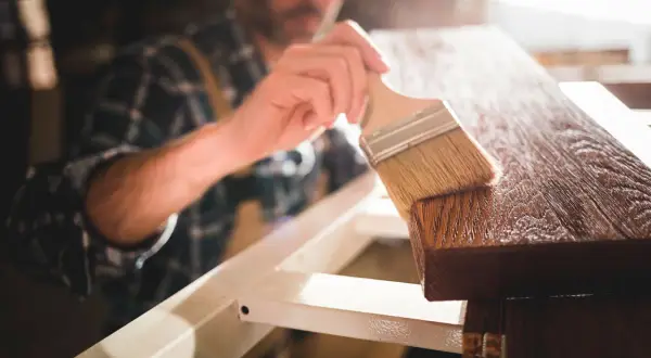 Un falegname applica una finitura su un pezzo di legno, esaltando le sue belle fibre del legno.