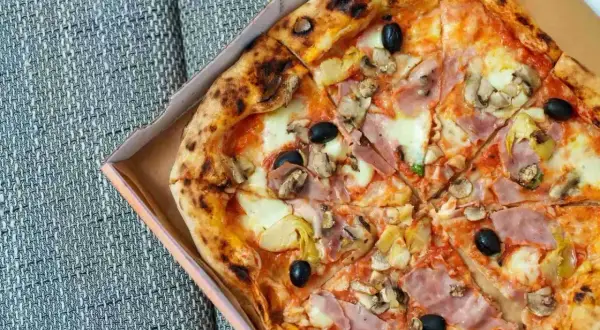 Pyszna pizza capricciosa z szynką, pieczarkami, karczochami i oliwkami w pudełku.