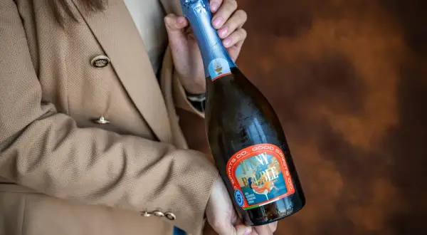 Kobieta w beżowym żakiecie trzyma butelkę musującego napoju, idealnego na międzynarodowy dzień prosecco.