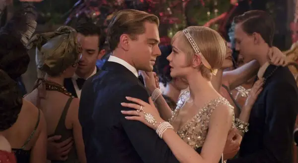 Para Gatsby'ego, taniec z Daisy to chwila magii. Ona w błyszczącej sukni, on w eleganckim garniturze, otoczeni gośćmi na przyjęciu.