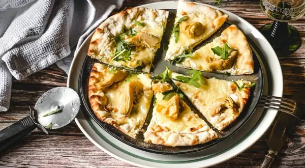 Eine köstliche Pizza Bianca mit Artischocken, Rucola und Pinienkernen, bereit zum Genießen.