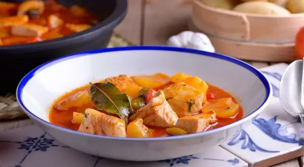 Un plato humeante de patatas con bonito, con trozos de pescado tierno y patatas en una salsa roja sabrosa, adornado con hojas de laurel.