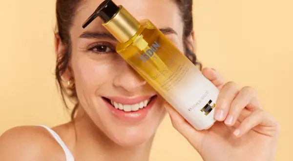 Mujer sonriente sostiene una botella de aceite de ducha ISDIN.