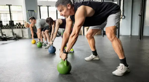 Gruppe trainiert Griffkraft mit Kettlebells. Sie heben die Gewichte vom Boden, um ihre Hände zu stärken.