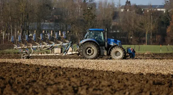 Niebieski traktor z pługiem orze pole. Rolnik przygotowuje ziemię, zastanawiając się, do kiedy można orać pole arimr.