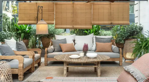 Acogedora terraza estilo mediterráneo con sofá, sillones de madera, mesa de centro y abundante vegetación.