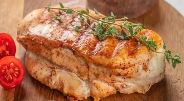 Soczysty, pieczony filet z indyka z gałązką tymianku i pomidorkami koktajlowymi na drewnianej desce.