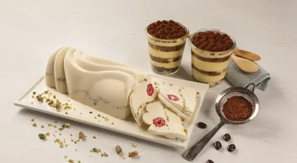 Delikatny krem do tortu z mascarpone, udekorowany malinami i pistacjami, obok deserów tiramisu.