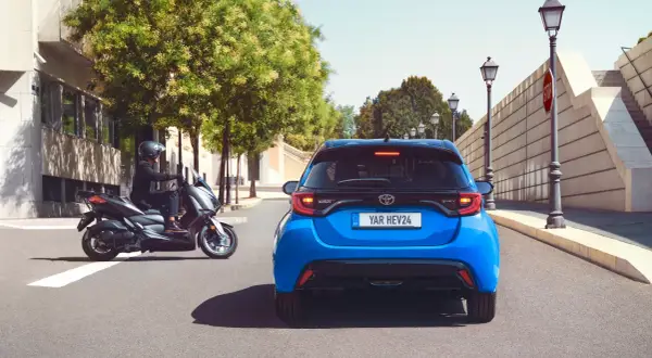 Niebieski Toyota Yaris HEV. Kierowca na skuterze obok. Szukasz "toyota yaris instrukcja obsługi po polsku"?