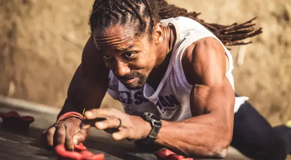 Man with dreadlocks on a climbing wall, his forearm punch showing determination as he grips the holds.