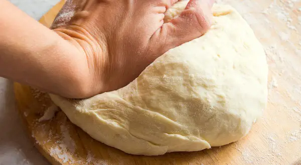 Main d'une personne pétrissant une pâte à pain sur une planche en bois. Une question se pose : pourquoi ma pâte ne lève pas ?