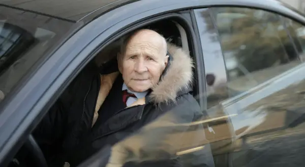 Un homme âgé, au regard vif, est assis au volant de sa voiture, prêt à prendre la route. Son permis de conduire senior lui permet de garder son indépendance.