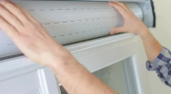 Mains manipulant un volet roulant blanc, étape clé pour savoir comment réparer un volet roulant.