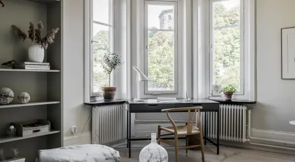 Scrivania con vista finestra, un angolo studio luminoso con sedia in legno e piante.