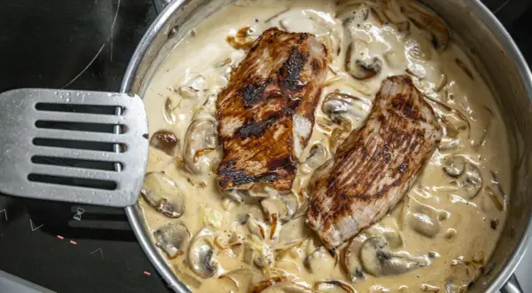 Dwa kawałki grillowanego mięsa w kremowym sosie pieczarkowym. Idealny przykład, jak zrobić sos pieczarkowy, który zachwyci smakiem.