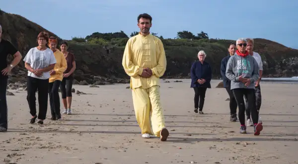 Un groupe suit un homme en tenue jaune lors d'une marche afghane sur une plage.