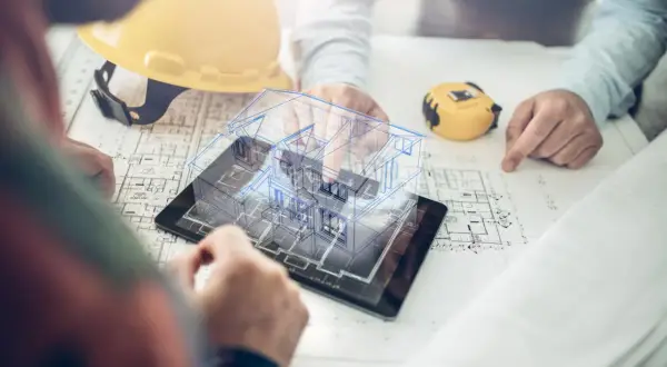 Dwie osoby analizują plany budynku i cyfrowy model domu na tablecie.