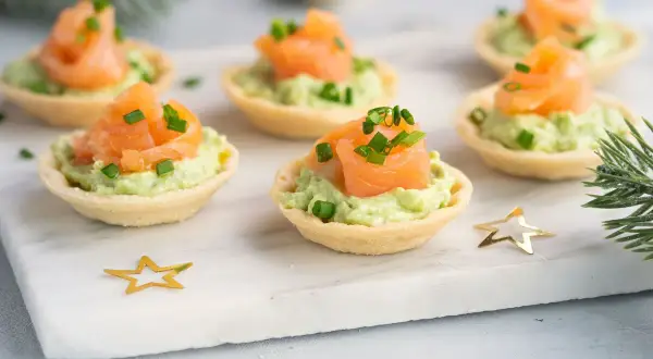Aperitivos baratos para mucha gente: canapés de salmón y aguacate, decorados con cebollino y estrellas doradas.
