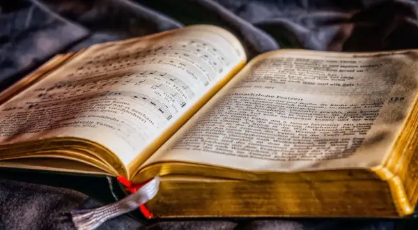 Otwarta księga z nutami i tekstem, symbolizująca motyw dobra i zła w literaturze.