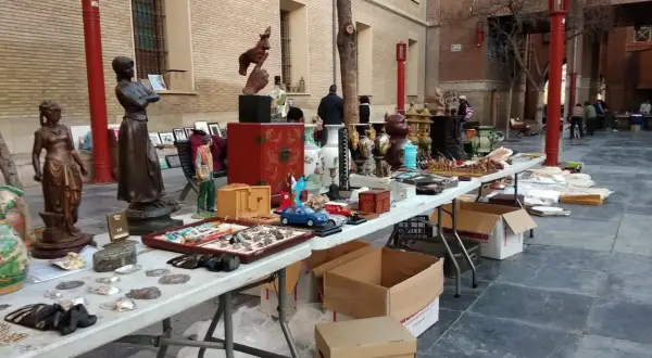 Mercado de antigüedades en Zaragoza con estatuas, jarrones y objetos curiosos en mesas al aire libre.