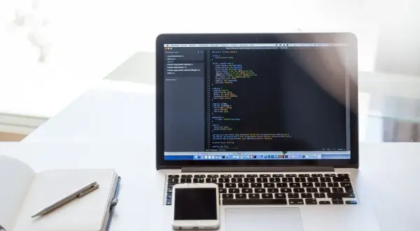 Laptop z kodem, telefonem i notatnikiem. Dobry laptop powinien mieć odpowiednie parametry do pracy.