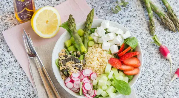 Un plat végétarien coloré avec du quinoa, des asperges, des fraises, du concombre, des radis, des graines et du fromage feta.