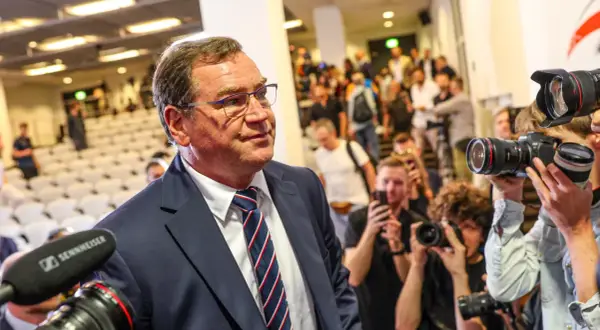 Mężczyzna w garniturze, jak kapitan reprezentacji Polski, otoczony przez fotoreporterów z aparatami.