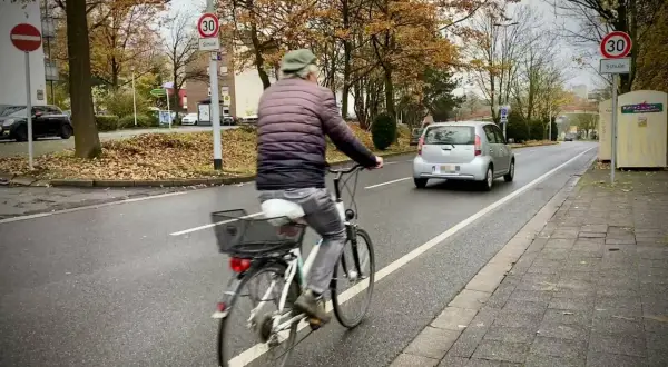 Mann fährt Rad auf einem geschützten Radweg. Ein Auto fährt auf der Straße.