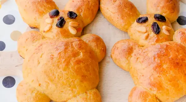Zwei goldbraune Osterhasen aus Hefeteig, dekoriert mit Rosinen und Mandeln. Perfekt zum Osterbacken mit Kindern.
