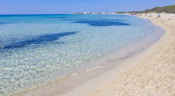 Spiaggia di Punta Prosciutto, Maldive del Salento. Acque cristalline e sabbia dorata sotto un cielo azzurro.