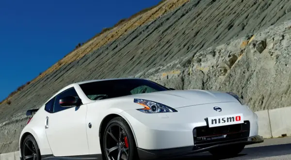 Biały Nissan 370Z Nismo z czerwonymi akcentami na lusterkach i zaciskach hamulcowych, zaparkowany na tle skalistego zbocza.