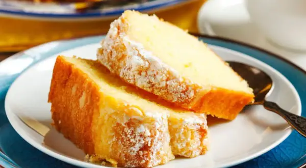Deux parts de gâteau au yaourt moelleux, saupoudrées de sucre glace, sur une assiette blanche avec une cuillère ornée.