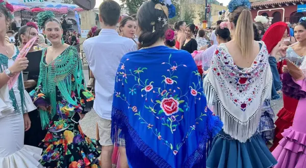 Mujeres con trajes de flamenca y mantones bordados, uno azul con flores rojas y otro blanco con detalles coloridos.