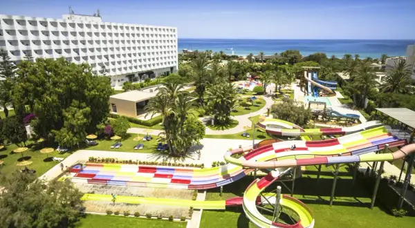 Kolorowy aquapark na plaży w Saharze, z hotelowcem w tle i błękitnym morzem.