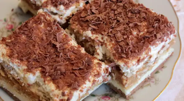 Pyszne ciasto krówka bez pieczenia, warstwowe, z kremem i posypką czekoladową, na ozdobnym talerzyku.