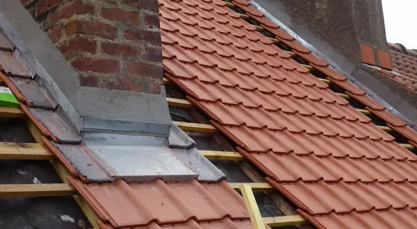 Dachdecker arbeiten am Schornstein, um ihn abzudichten. Neue rote Dachziegel werden verlegt.