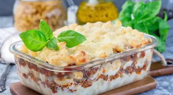 Zapiekanka makaronowa z mięsem mielonym i kremowym sosem, udekorowana bazylią.