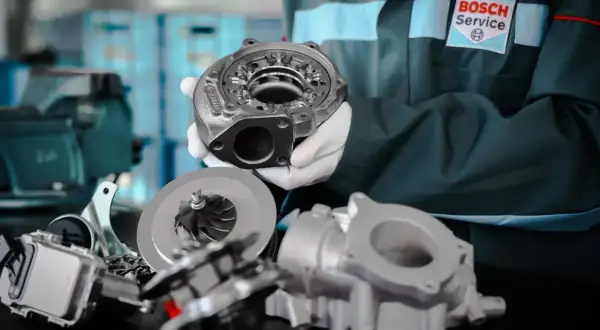 Mechanik w rękawiczkach prezentuje turbosprężarkę, kluczowy element dla wydajności silnika wolnossącego.