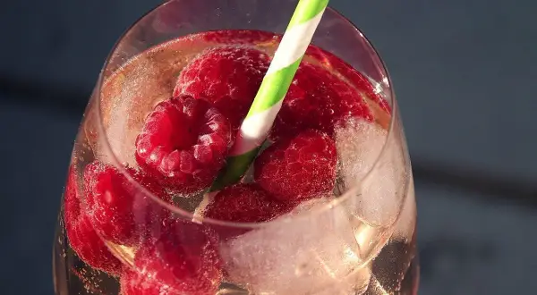 Erfrischender Pfirsich Spritz mit Himbeeren und Eiswürfeln in einem Glas, bereit zum Genießen.