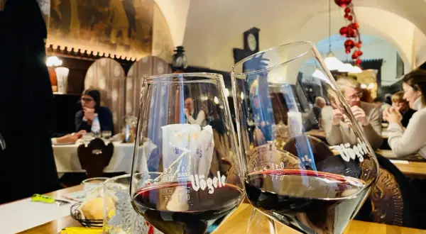 Dwa kieliszki pełne ciemnoczerwonego lagrein wino, w tle restauracja z ludźmi i świątecznymi ozdobami.