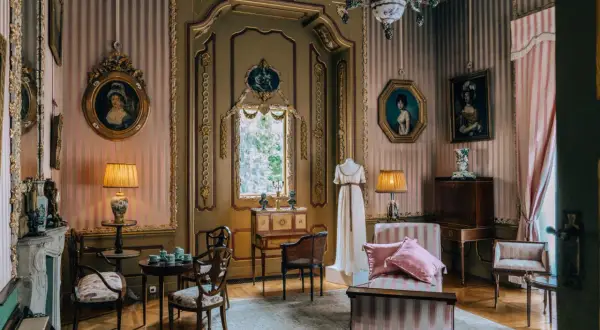 Eleganckie wnętrze pałacu w Nieborowie. W pokoju z różowo-białymi pasami na ścianach, obrazy, meble i manekin w sukni.
