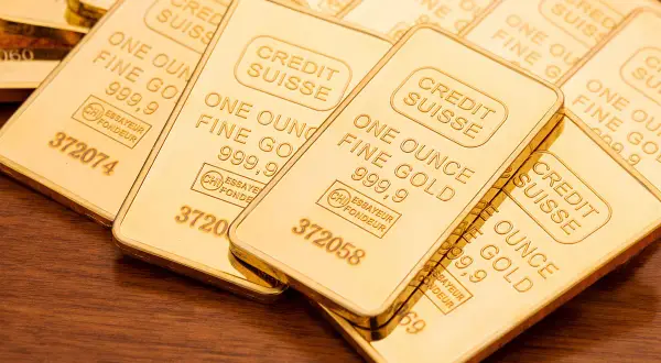 Sztabki złota Credit Suisse, każda o wadze jednej uncja trojańska, błyszczą na drewnianym tle.