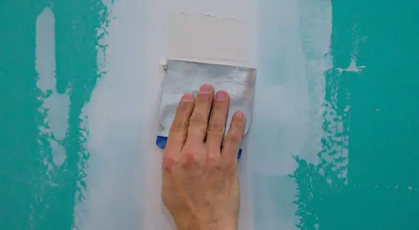 Main d'un artisan ponçant un mur à la main avec une spatule pour lisser le plâtre.
