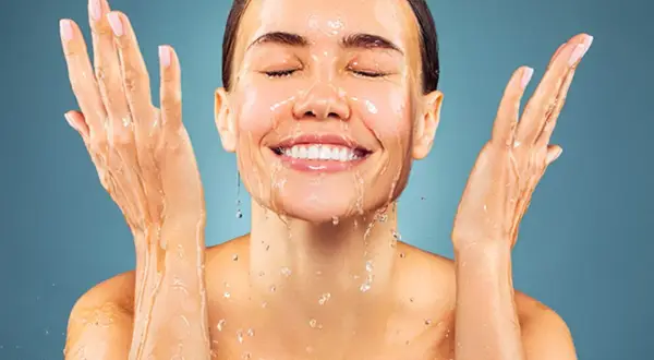 Donna sorridente con acqua sul viso e mani. L'acqua micellare a cosa serve? A detergere e rinfrescare la pelle.